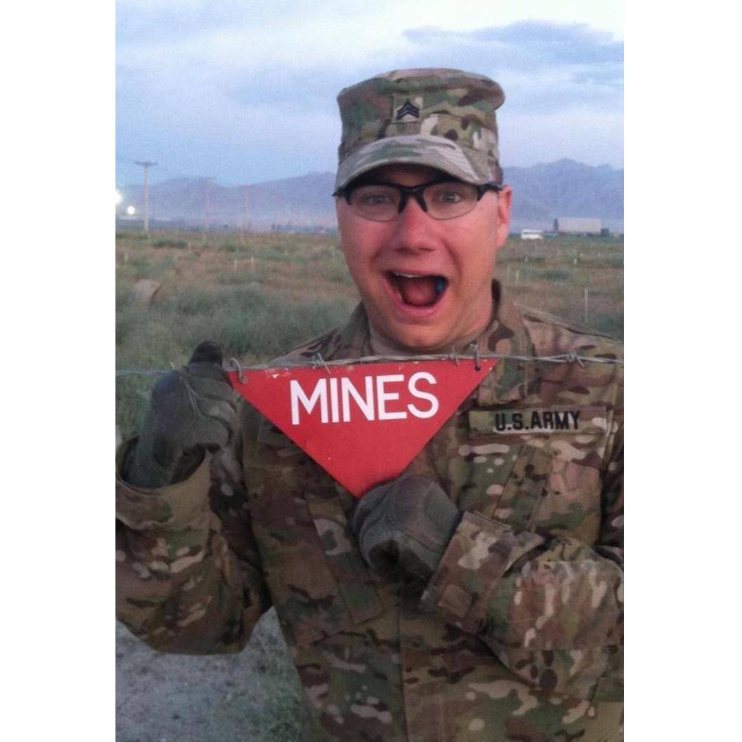 Rob Kumph in uniform and smiling while holding a flag that says Mines